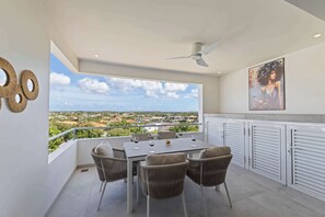 A balcony with a table and chairs, a ceiling fan, and a view of the landscape. - Palm Paradise-Stylish Island Live-Blue Bay Curaçao (Willemstad)