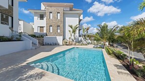A modern pool area with a clear blue pool, surrounded by a white building with stone accents and palm trees. - Palm Paradise-Stylish Island Live-Blue Bay Curaçao (Willemstad)