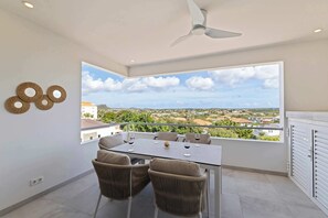 A balcony with a table and chairs, a ceiling fan, and a view of a residential area. - Palm Paradise-Stylish Island Live-Blue Bay Curaçao (Willemstad)