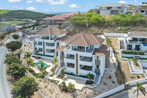 Un complejo residencial moderno con varias casas de dos pisos, una piscina y un paisaje montañoso al fondo.
