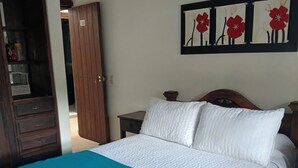 A bedroom with a bed, a nightstand, a wooden wardrobe, and a wall with three red flower paintings.