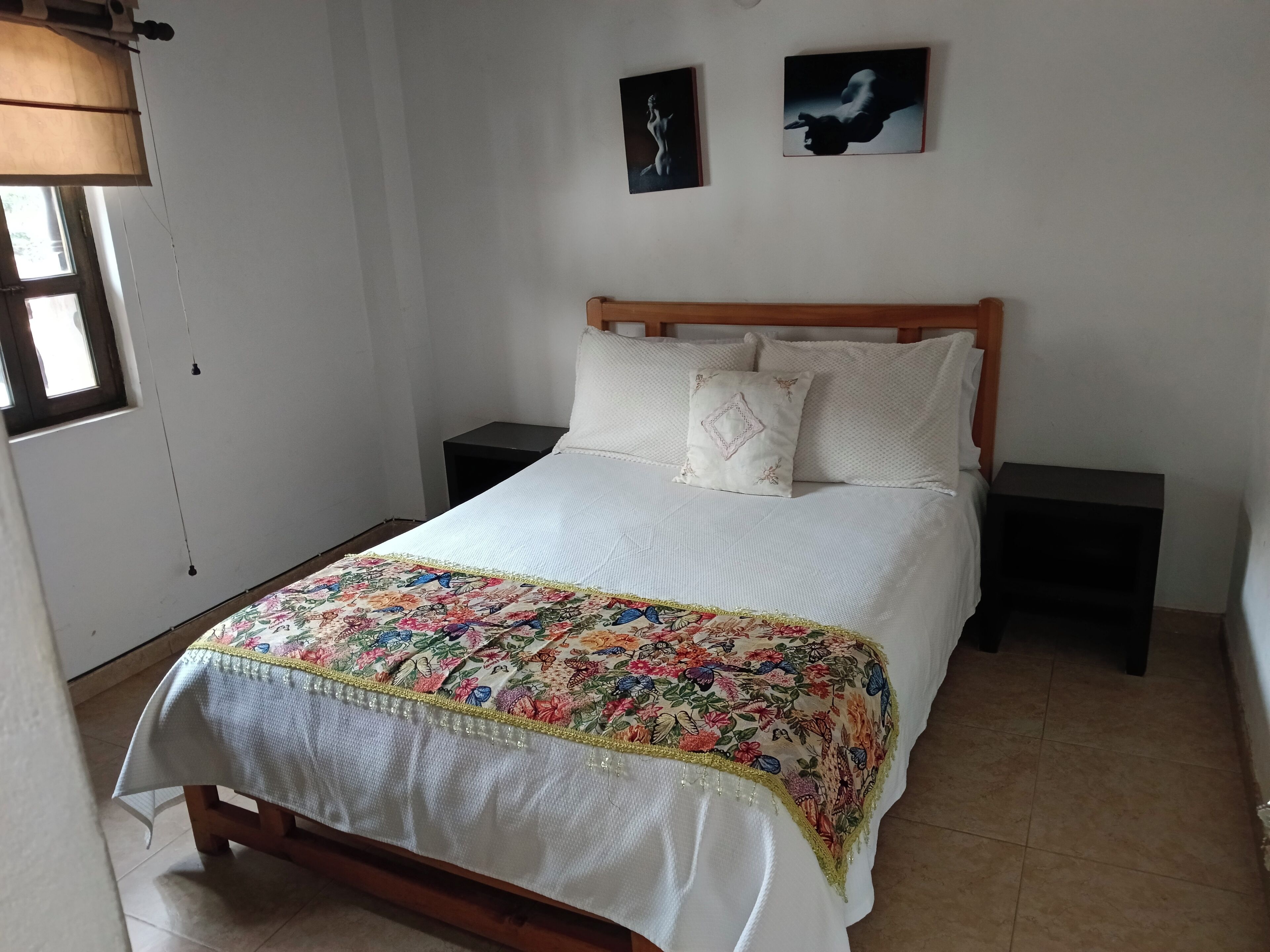 A bed with a floral bedspread, two nightstands, and two wall-mounted artworks.