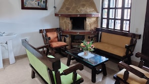 A living room with a stone fireplace, wooden furniture, a painting, and a window with multiple panes.