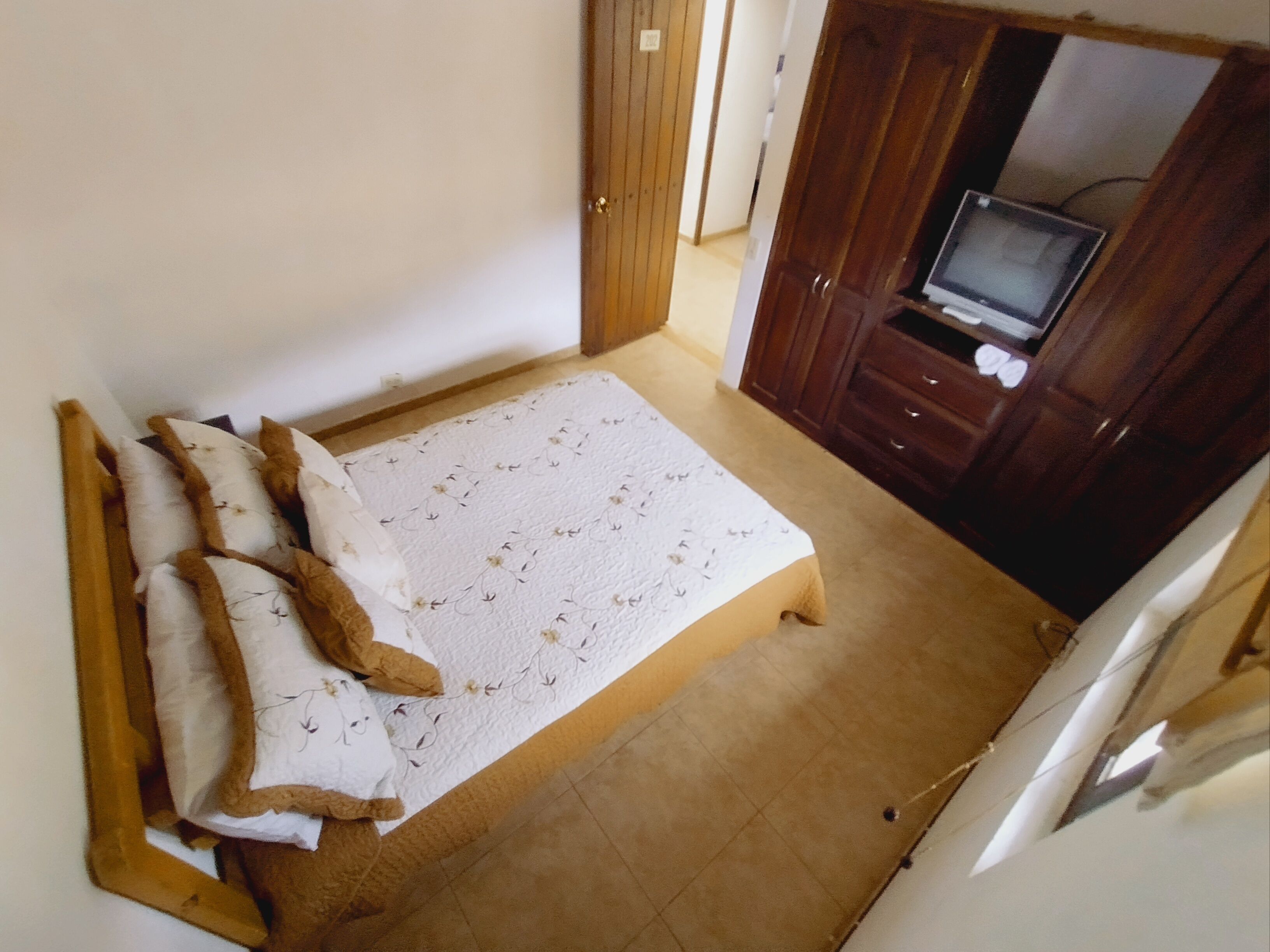 A bedroom with a bed, a television on a stand, and a wardrobe.