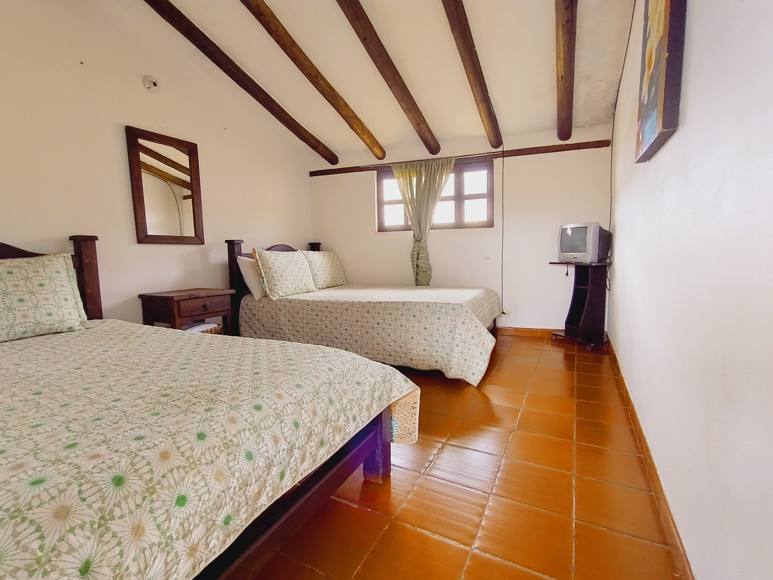 A bedroom with two beds, a TV, and a window with curtains.