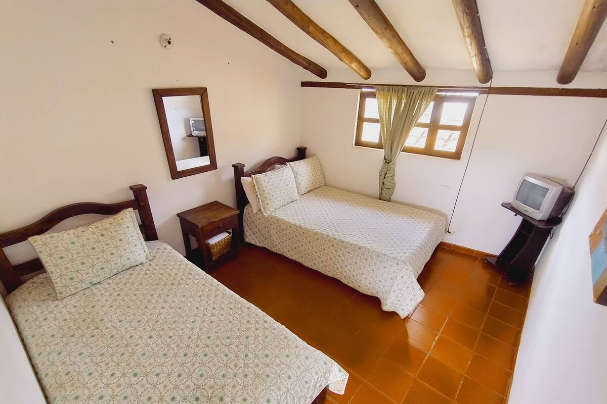 A room with two beds, a small table, a television, and a window with curtains.