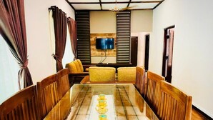A dining area with a long table, wooden chairs, and a television mounted on the wall.