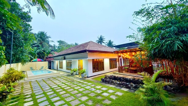 A modern house with a swimming pool, a covered outdoor area, and lush greenery.