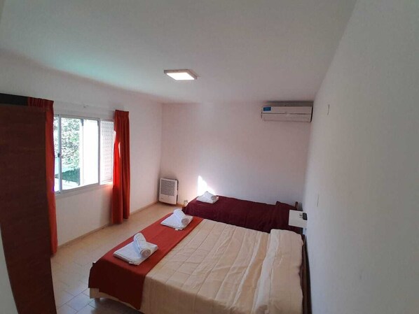 A room with two beds, a window with curtains, a ceiling light, and an air conditioning unit. - HOTEL CRISTAL (Villa Carlos Paz)