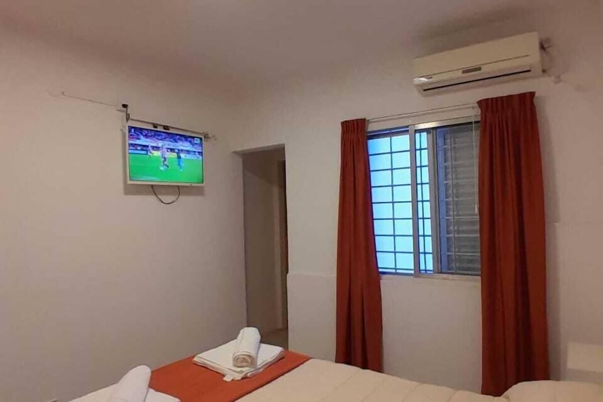 Een hotelkamer met een bed, een televisie aan de muur, een airconditioner en een raam met gordijnen.