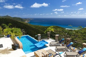 Una piscina en la azotea con tumbonas azules y vista al océano.