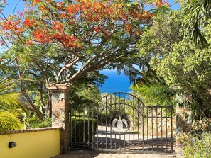 A gated entrance with a metal gate, a brick pillar, and a view of the sea.