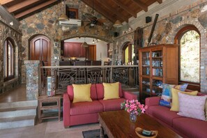 A stone-walled interior with a red sofa, wooden coffee table, and a bookshelf.