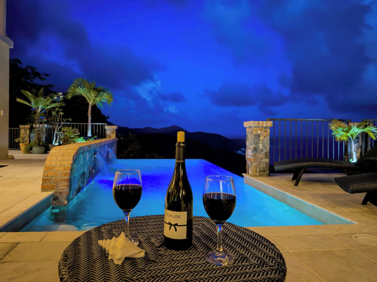 En flaske vin og to glas på et bord ved en pool med udsigt til bjergene.