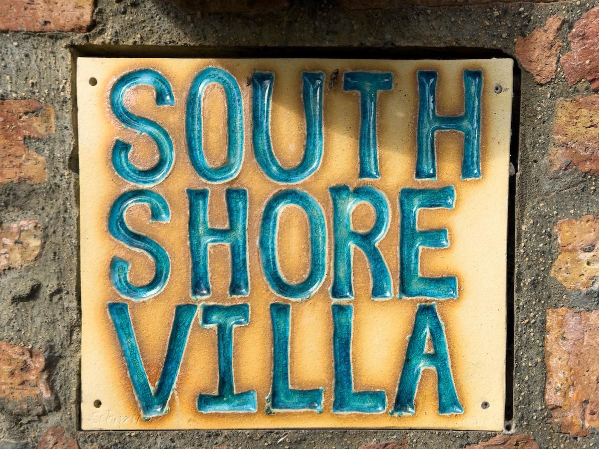 Placa com o texto 'SOUTH SHORE VILLA' fixada em uma parede de tijolos.