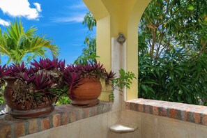 A balcony with potted plants, a small white stool, and a yellow wall.