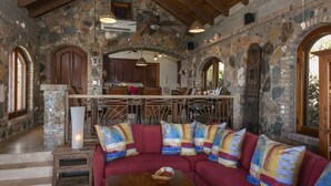 A stone-walled interior with a red sectional sofa, wooden dining table, and arched doorways. - South Shore Villa, SolVillasUSVI (Cruz Bay)