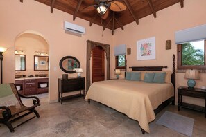 A bedroom with a large bed, a vanity with a mirror, and a window with a view of trees.