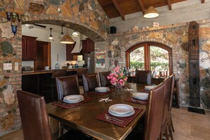 A stone-walled dining area with a large table set for six, surrounded by leather chairs.