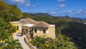 A yellow villa with a tiled roof, surrounded by lush greenery and hills. - South Shore Villa, SolVillasUSVI (Cruz Bay)