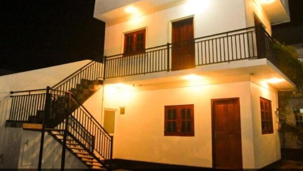 Un edificio de dos pisos con un balcón en el nivel superior, una escalera que conduce al piso de arriba, y una puerta en la planta baja.