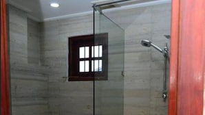Cabina de ducha con vidrio, un inodoro y un ventanal pequeño.