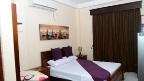 Una habitación de hotel con cama, mesita de noche, un cuadro y una ventana con cortinas.