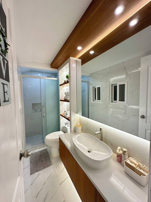 Un baño moderno con un espejo grande, un tocador con lavamanos y una zona de ducha.