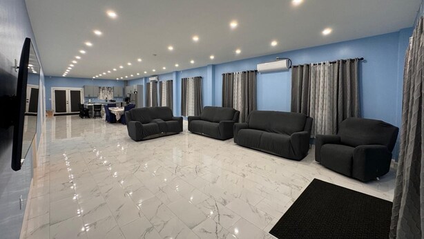 A spacious living area with a kitchen in the background, a flat-screen TV mounted on the wall, and a ceiling with recessed lighting. - 4-bedroom house in nice Georgetown with WiFi, AC. Enjoy your stay (Georgetown)