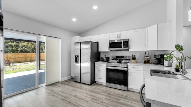 Une cuisine moderne dotée d’appareils électroménagers en acier inoxydable, de meubles blancs et d’une grande porte-fenêtre coulissante donnant sur un jardin.