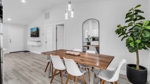 Un espace repas moderne avec une table en bois, des chaises blanches, un grand miroir et une plante en pot.
