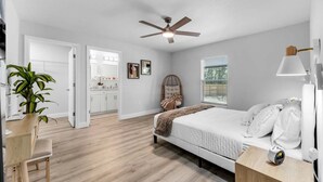 Une chambre à coucher comprenant un lit, une table de chevet, une lampe, un ventilateur de plafond et une fenêtre avec des stores.
