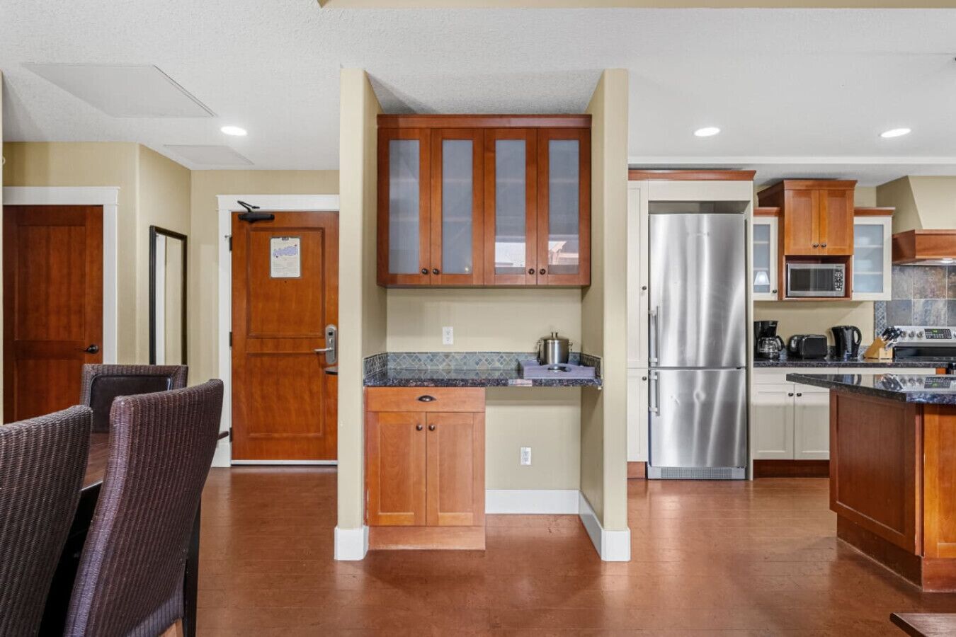 A modern kitchen with wooden cabinets, a stainless steel refrigerator, and a dining area with wicker chairs.
