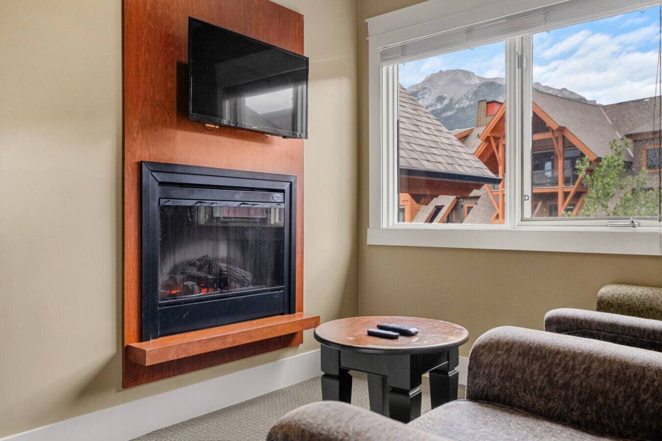 A cozy room with a fireplace, a television mounted above it, and a window offering a view of a mountain lodge.