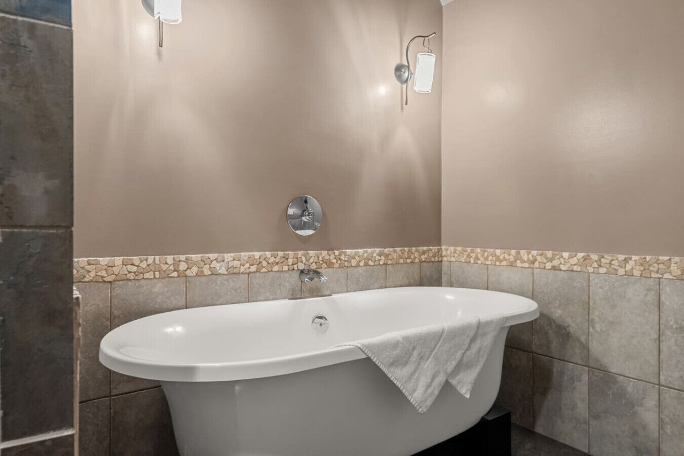 A bathroom with a freestanding bathtub, a wall-mounted mirror, and a towel on the tub.