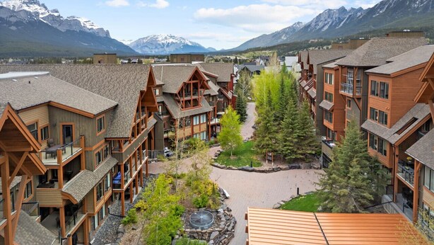 A lodge with multiple wooden buildings, a central courtyard with trees, and a mountain backdrop. - Rockies Base: Hot Tub, Pool & National Park Pass (Canmore)