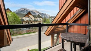 A balcony with a wicker chair, overlooking a street with houses and mountains in the background. - Rockies Base: Hot Tub, Pool & National Park Pass (Canmore)