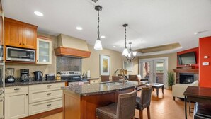 A modern kitchen with a central island, bar stools, a microwave, stove, and a dining area with a TV. - Rockies Base: Hot Tub, Pool & National Park Pass (Canmore)