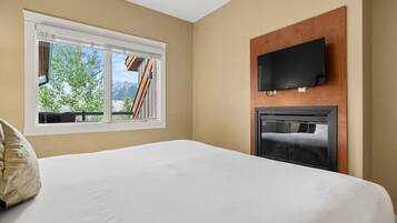 A hotel room with a bed, a TV mounted on a wooden panel, and a window with a mountain view.