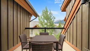 A balcony with a table and four chairs, wooden walls, and a view of trees and mountains. - Free Park Pass, Fireplace, Solara Resort Amenities (Canmore)