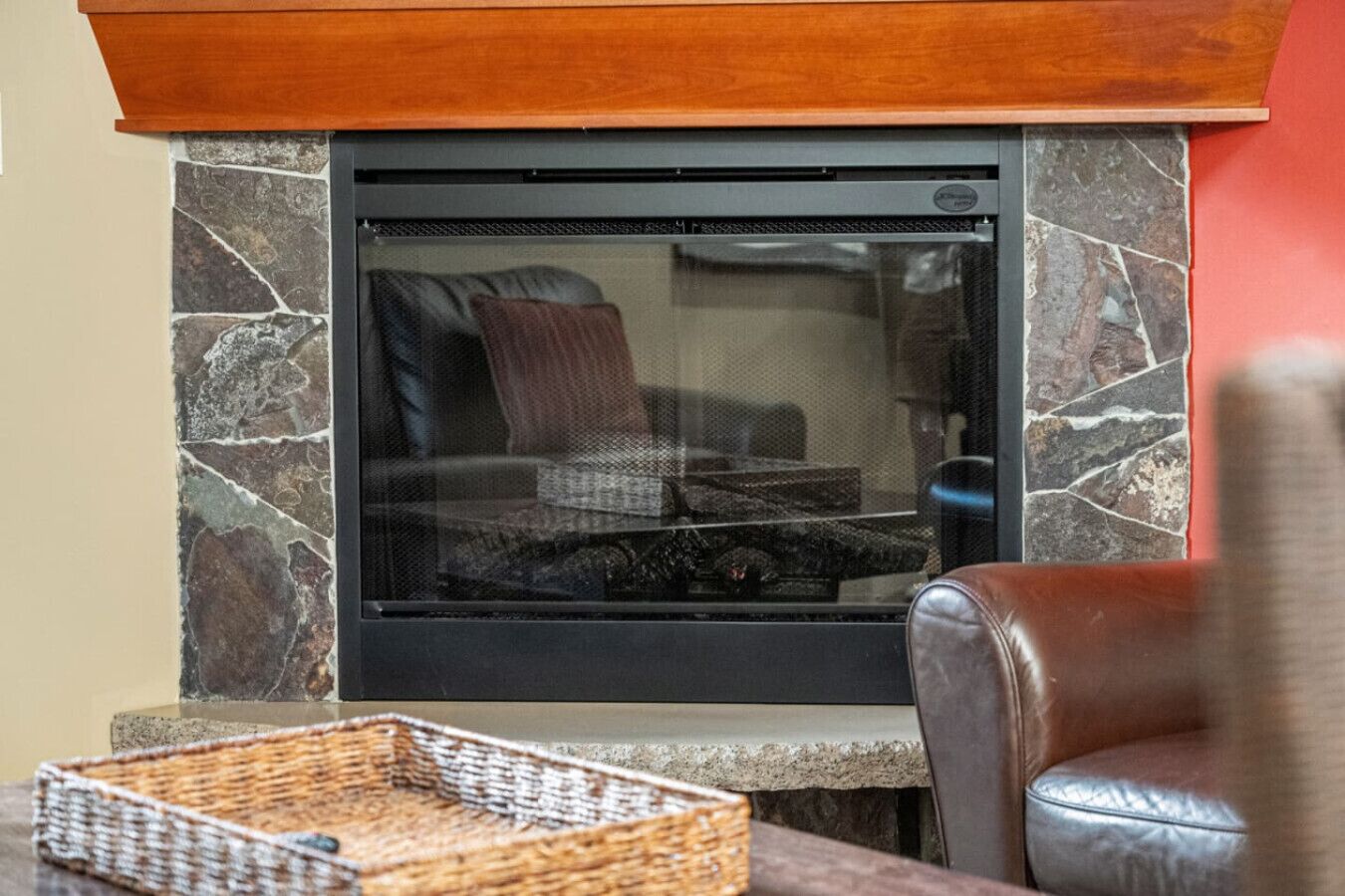 A stone fireplace with a glass screen, a leather chair, and a woven basket on a table.