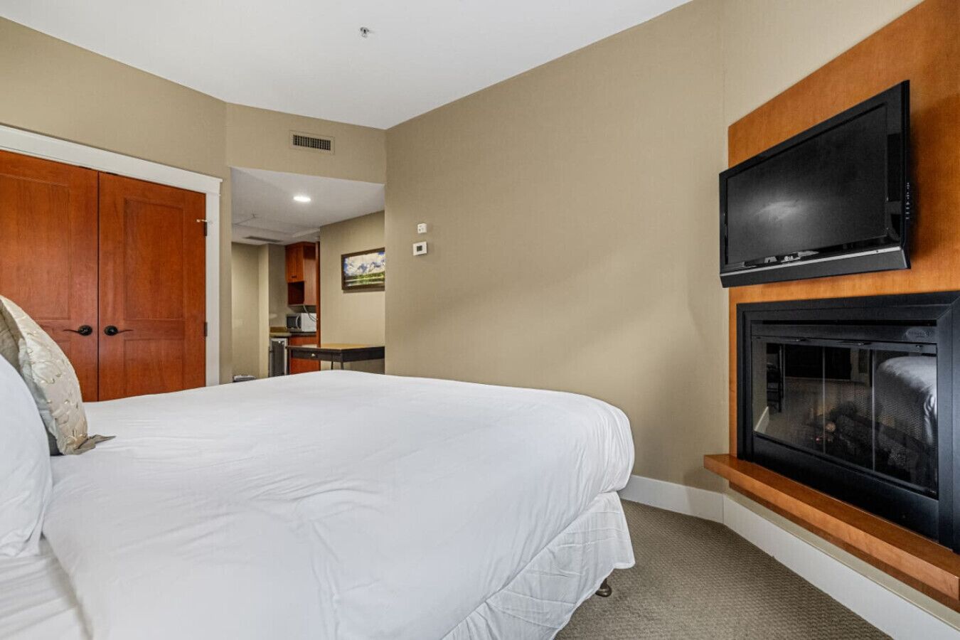 A hotel room with a large bed, a television mounted above a fireplace, and a wooden wardrobe.