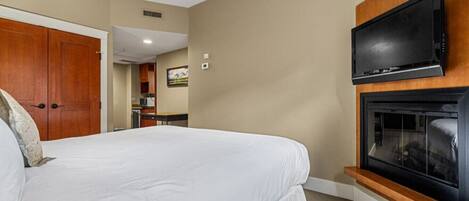 A hotel room with a large bed, a television mounted above a fireplace, and a wooden wardrobe.