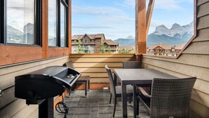 A patio with a grill, wicker table, and chairs, overlooking a mountain landscape. - Three Sisters View with Hot Tub, Pool & BBQ (Canmore)