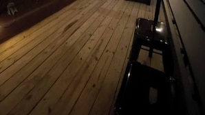 Una terraza de madera con un ventilador de techo, una banca y una mesa.