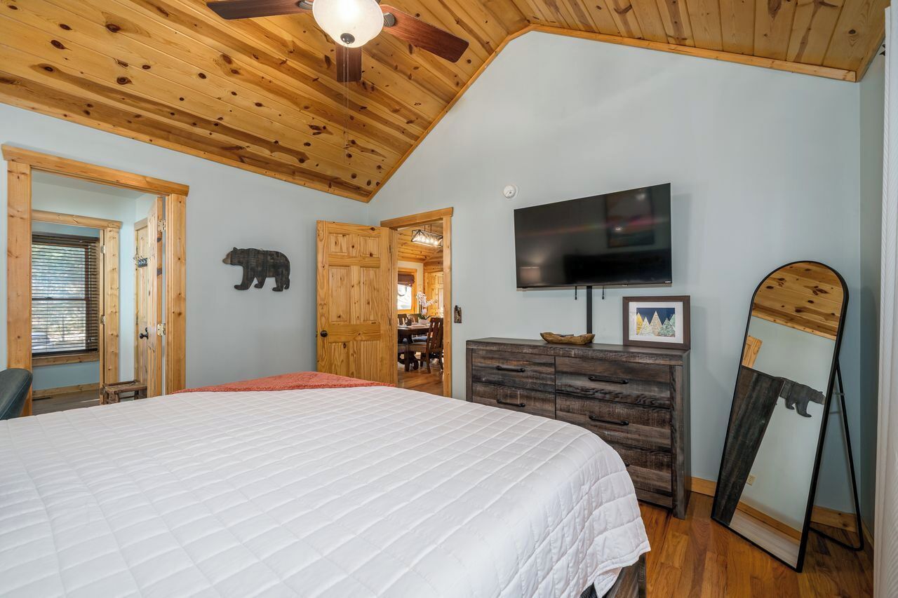 Un dormitorio con una cama grande, techo de madera, un televisor, un aparador y una decoración con un oso.