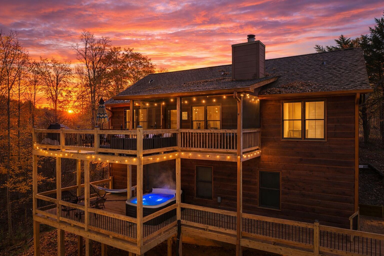 Una cabaña de madera de dos pisos con un jacuzzi en la planta baja y luces colgantes en el balcón.