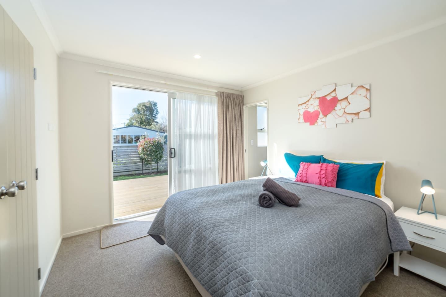 Quarto com cama grande, mesa de cabeceira, abajur e porta de vidro que se abre para área externa.