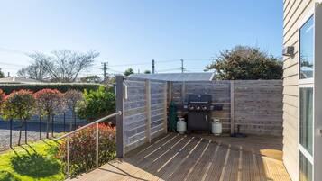Una terraza de madera con una parrilla y tanques de propano, rodeada por una valla de madera y un seto.