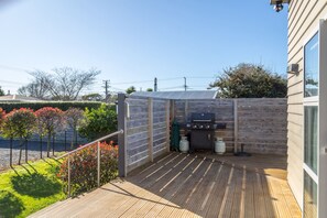 A wooden deck with a barbecue grill and propane tanks, surrounded by a wooden fence and a hedge.